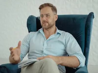 A man in a blue shirt gestures while talking in a coaching-style conversation.